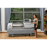 Woman standing next to Macy-Pan HP1501 hyperbaric oxygen therapy chamber in a modern room.