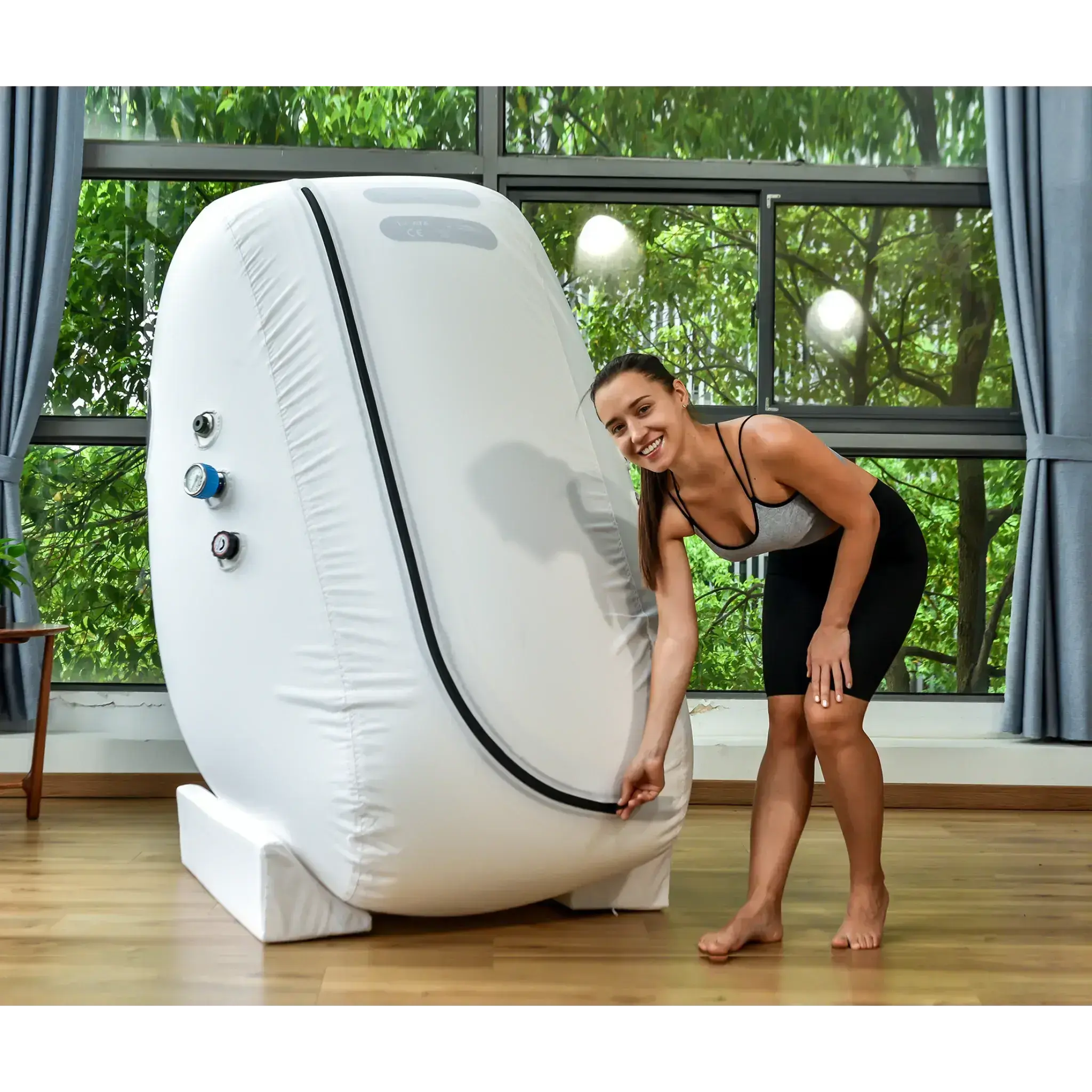 Woman adjusting the zipper of a Macy-Pan L1 Seated Hyperbaric Oxygen Therapy Chamber in a bright room.