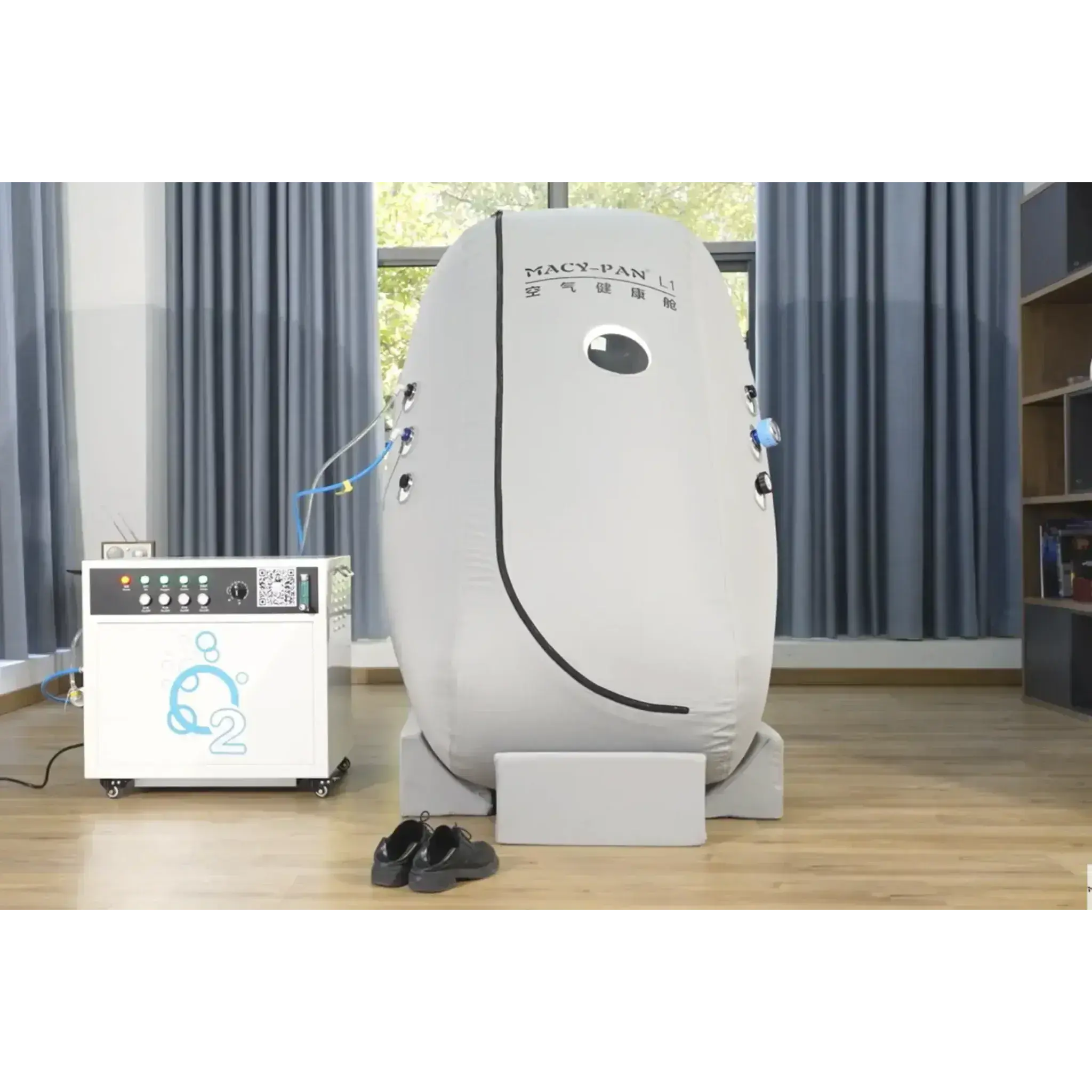 Macy-Pan L1 seated hyperbaric oxygen therapy chamber next to O2 generator in a bright room.
