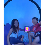 Two children relaxing inside a Newtowne 54" tent hyperbaric chamber, with a tablet displaying colorful content.