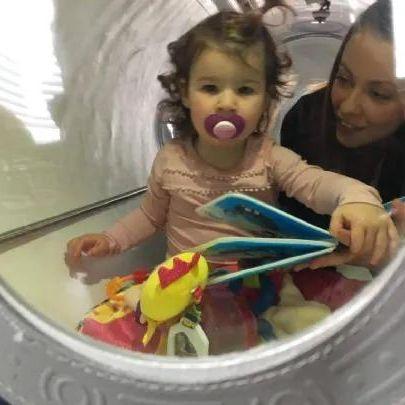 Baby inside oxynova 7 soft shell hbot chamber with pacifier and parent nearby.