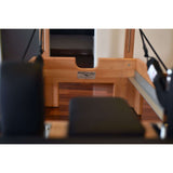 Close-up of the Private Pilates foldable metal reformer showcasing the wooden frame and padded seat.