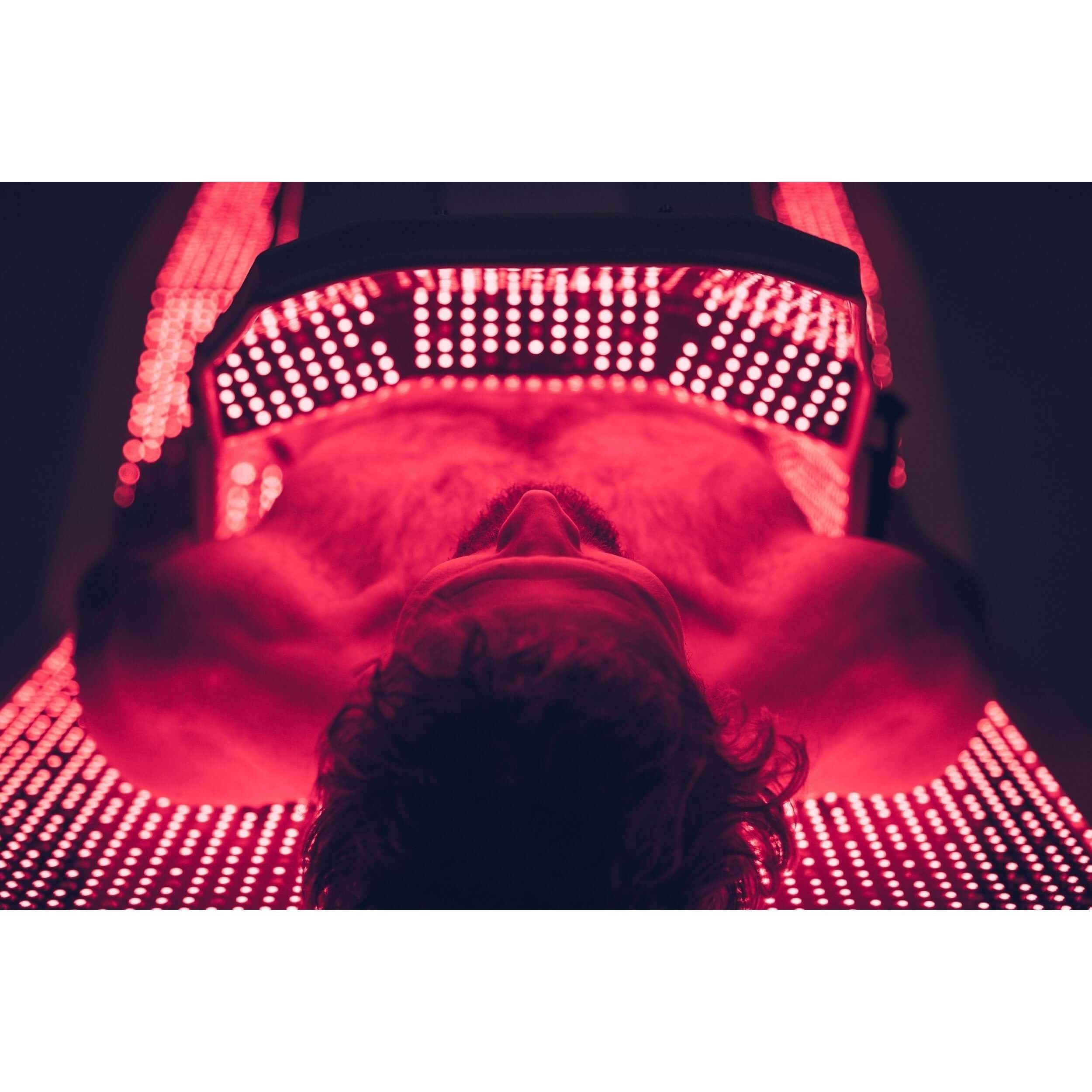 Male model lying on OvationULT Red Light Therapy Bed by Body Balance System, viewed from above showing zero-gravity positioning and contoured design