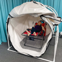 An interior view of the large Summit To Sea Grand Dive Pro Plus Hyperbaric Machine. The front is unzipped and a woman rests in a lounger inside